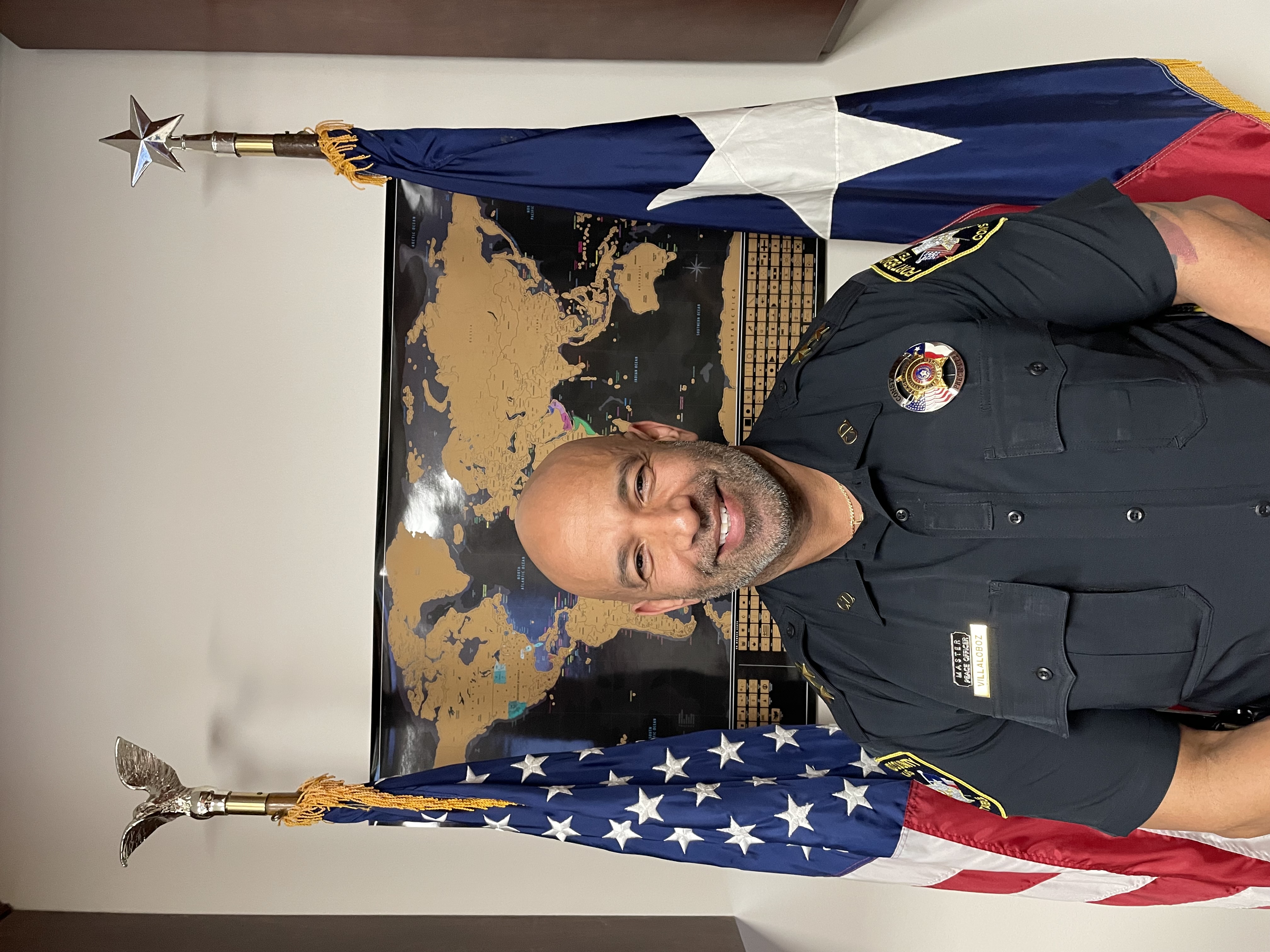Assistant Chief Villaloboz standing for picture in front of flags & a map